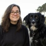 Female wearing glasses posing next to a furry black and white dog
